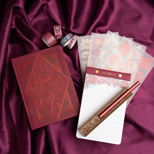Stationery items including a red notebook, pen, and stationery set on a purple fabric background