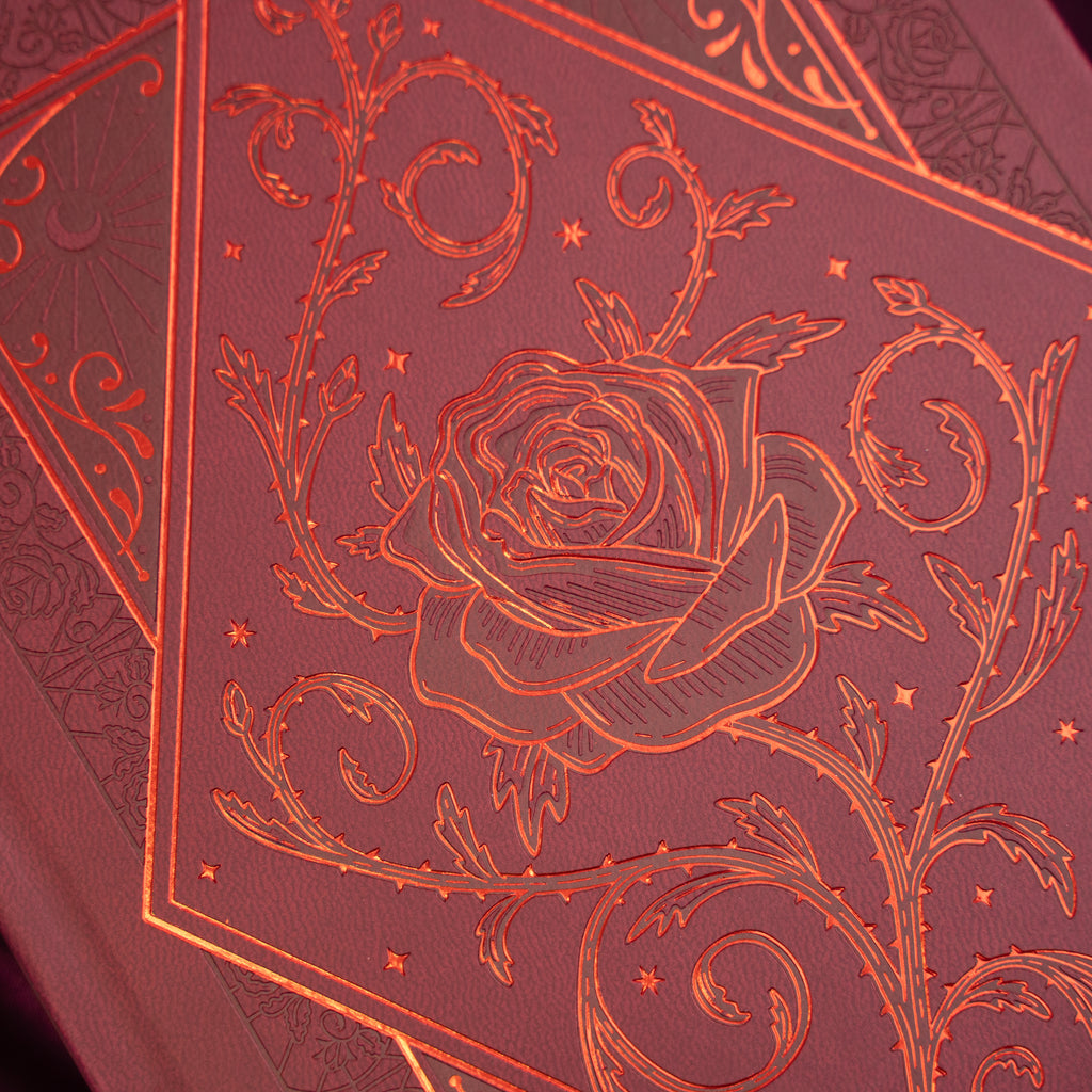 Close-up of a red notebook with intricate floral design and rose embossing.