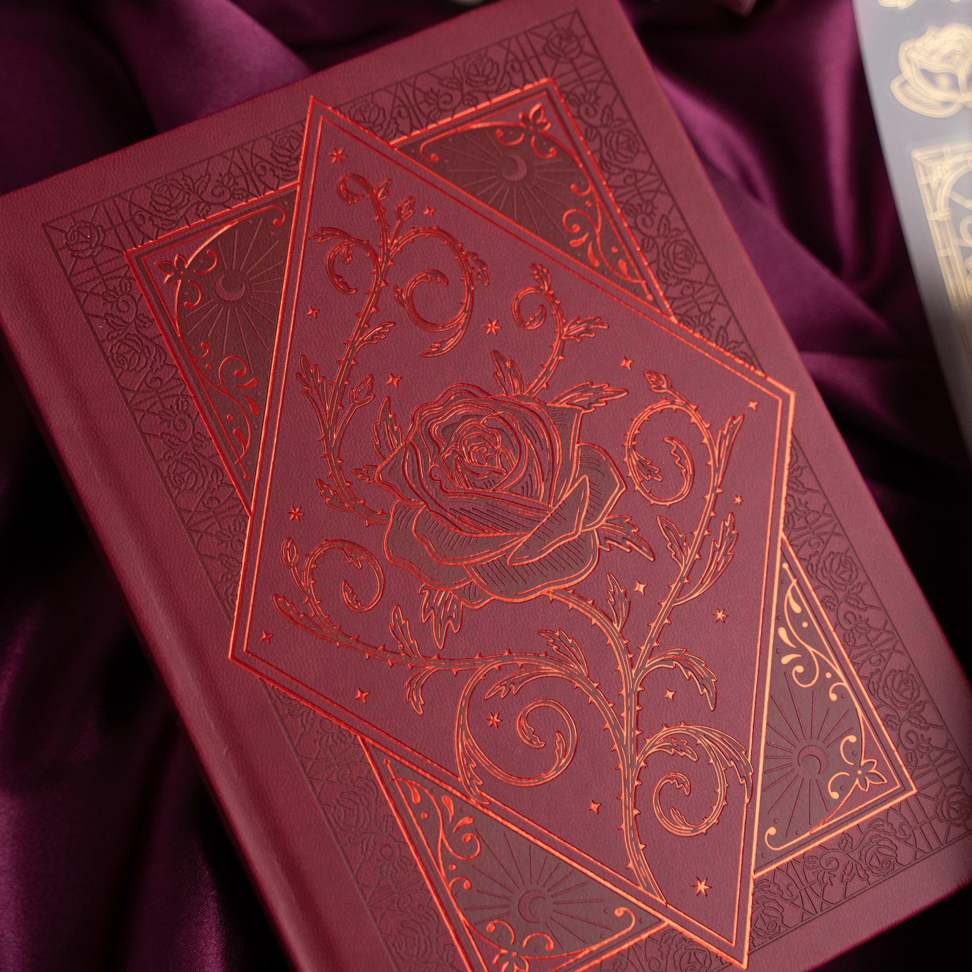 Red leather-bound book with intricate rose design on a purple fabric background